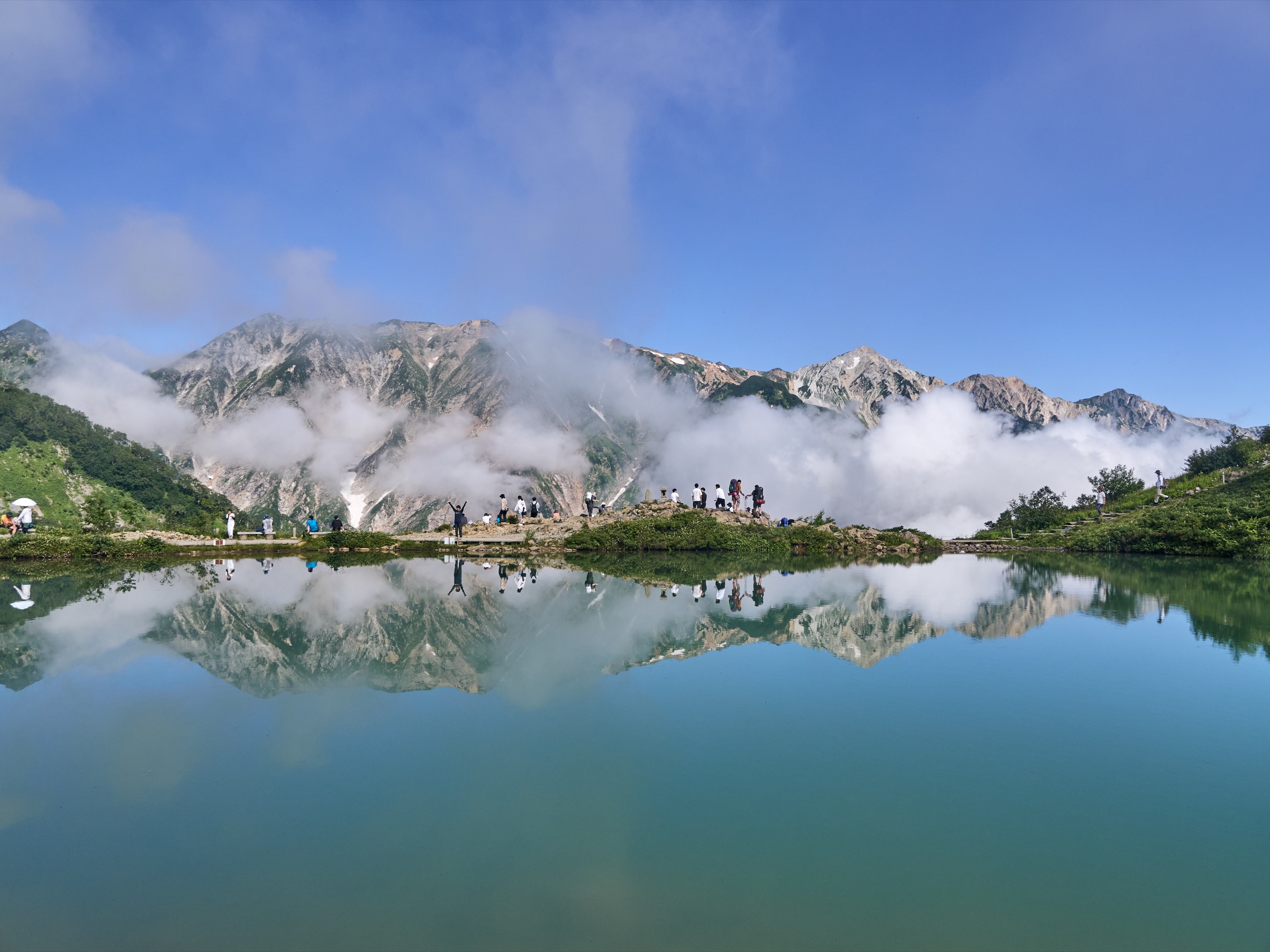 Hikers gathered beside a reflective alpine pond in summer