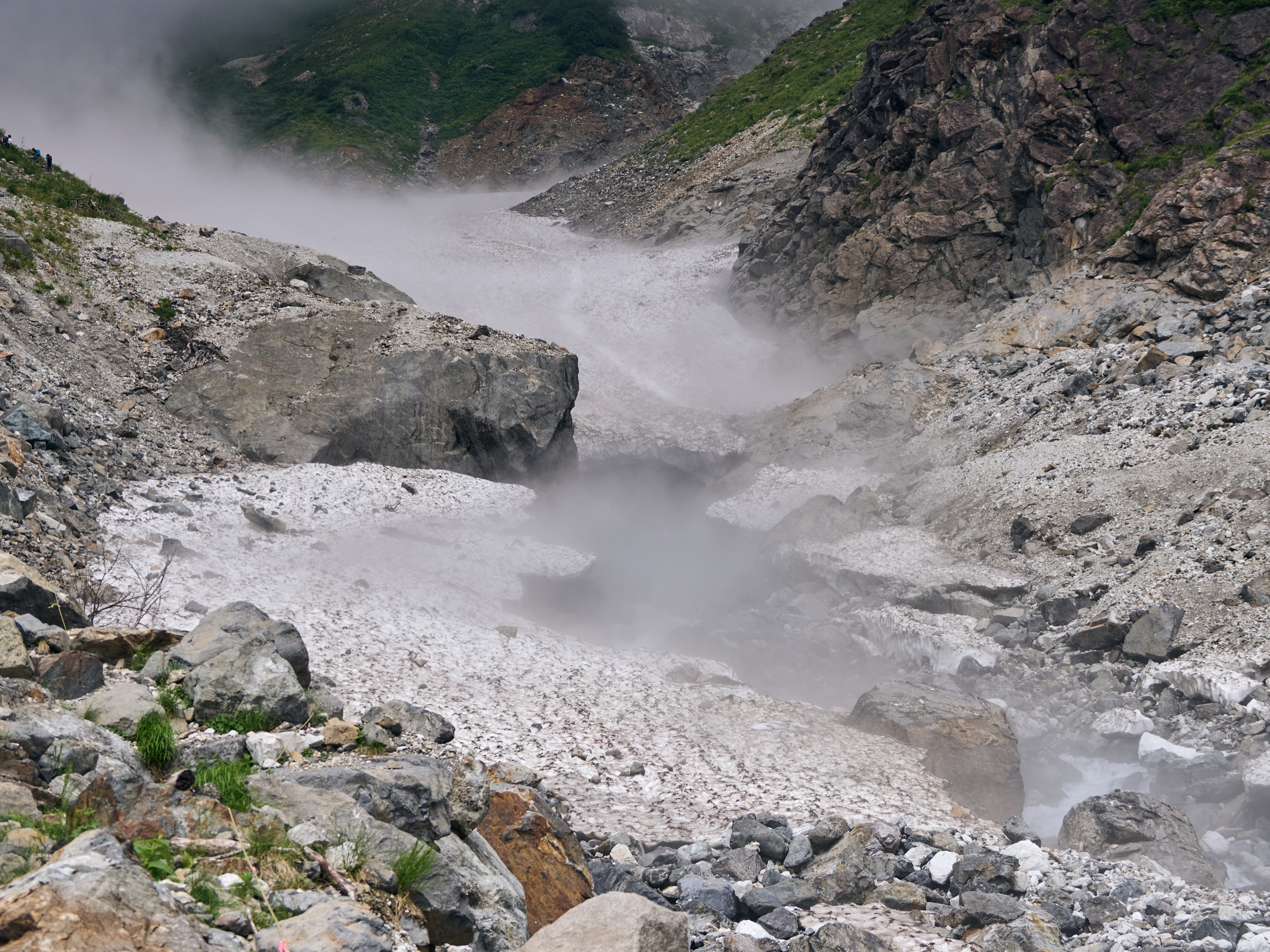 Meltwater running below a band of residual snow in summer terrain