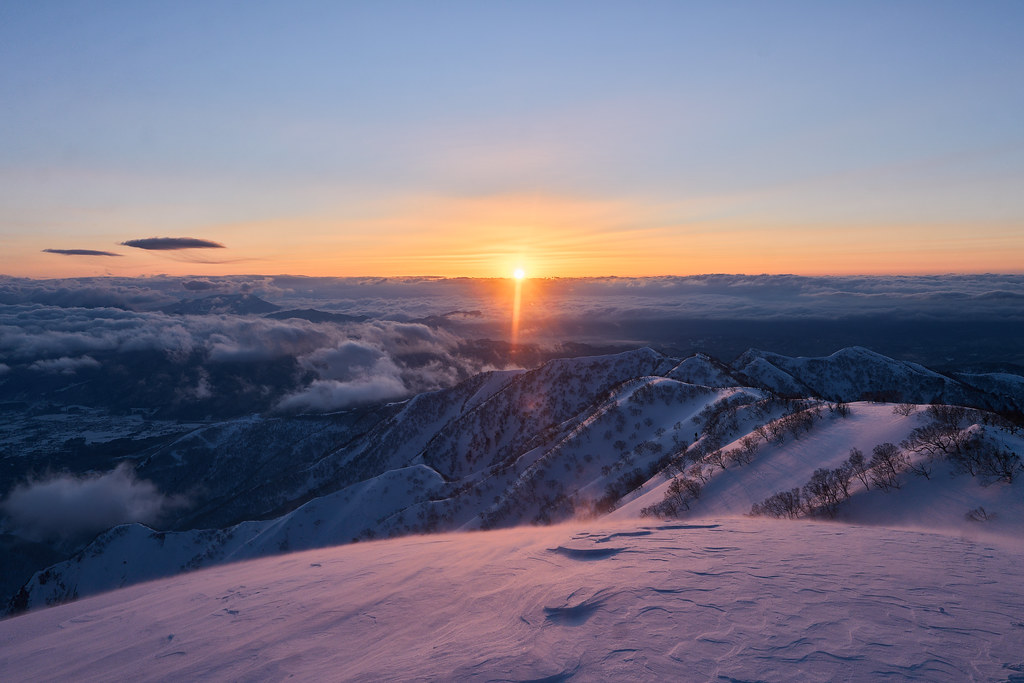 The setting sun casting warm light across the snowfields of Hakuba