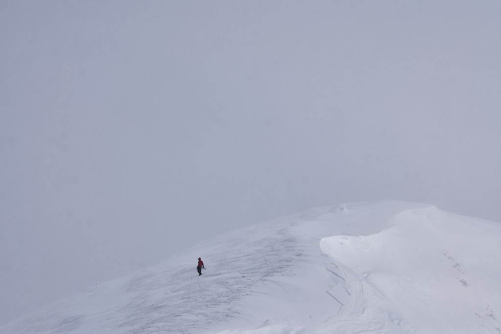 A lone climber moving across a snow ridge in whiteout conditions